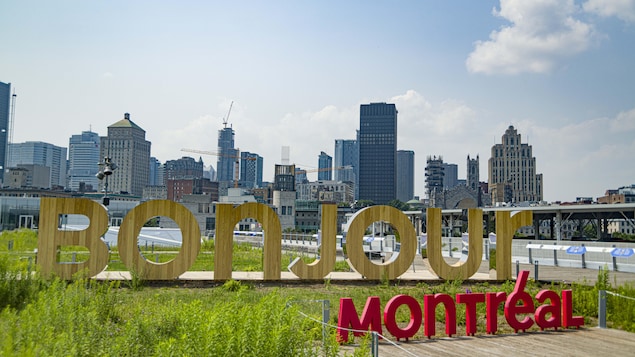 « Bonjour Montréal » érigé en lettres géantes dans un parc avec, en toile de fond, le centre-ville de Montréal.