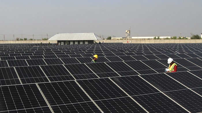 Deux personnes portant un casque de sécurité marchent entre les rangées de panneaux solaires dans un grand parc photovoltaïque