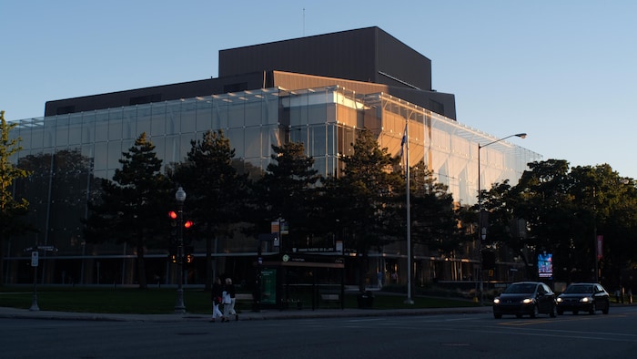 Un grand bâtiment vitré, entouré de rangés d'arbre.