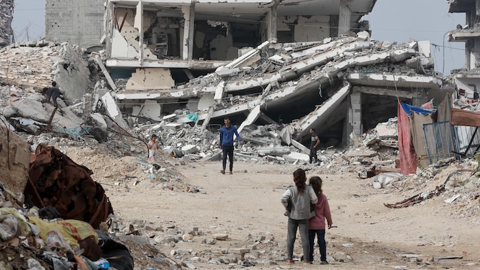 Deux hommes et quelques enfants marchent à travers les ruines d'immeubles détruits.