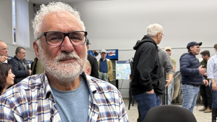 Un homme avec lunettes et barbe regarde la caméra.