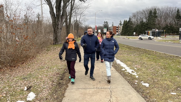 Trois personnes marchant dans un groupe en discutant sur un trottoir.